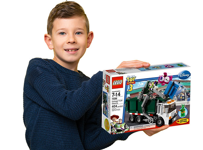 Young boy holding a LEGO recycling truck set, part of the complete collection of LEGO garbage and recycling truck sets released over the years.