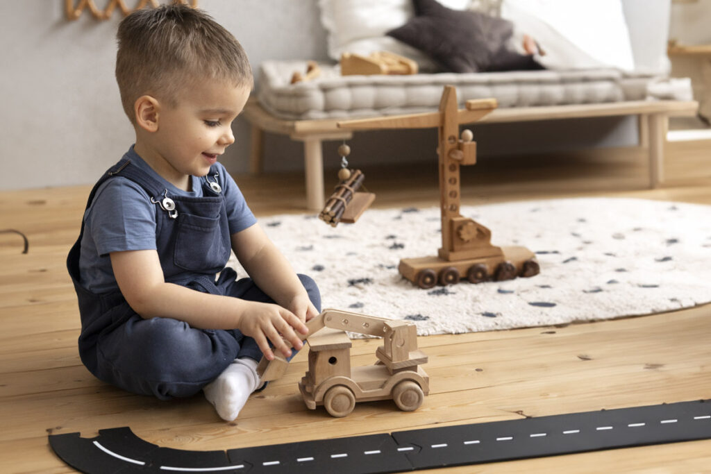 Young boy playing on the floor with wooden crane while showing what children can learn from truck play